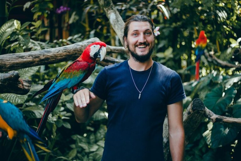 chico-joven-posando-zoologico-loro-mano-hombre-barbudo-pajaro_1296-778